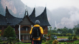 A hiker stands in front of an old asian building. Misty mountains in the background.